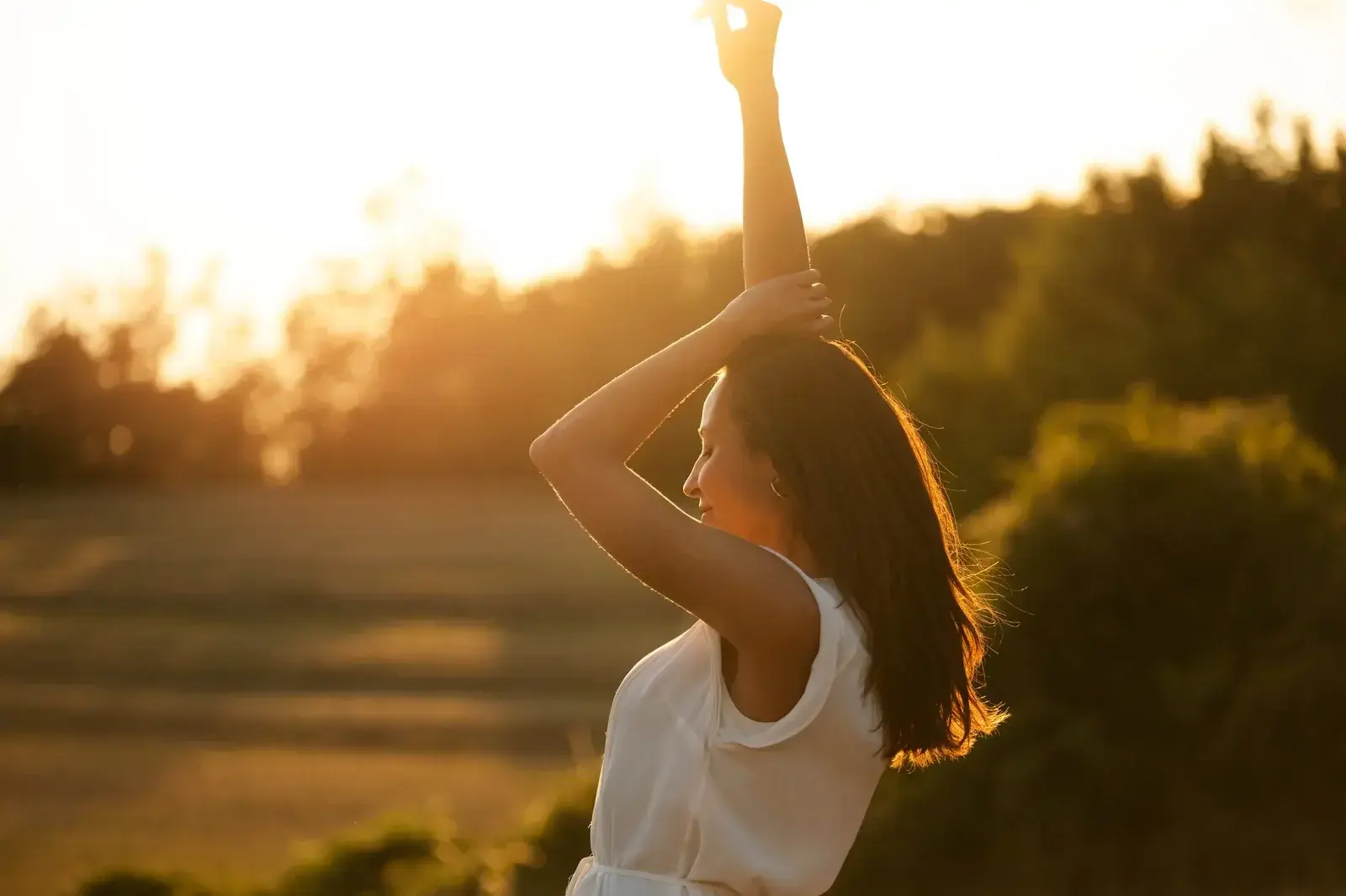 Mujer estirándose con el sol de fondo.